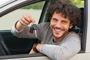 Young man sitting in car, smiling and holding up a set of keys.